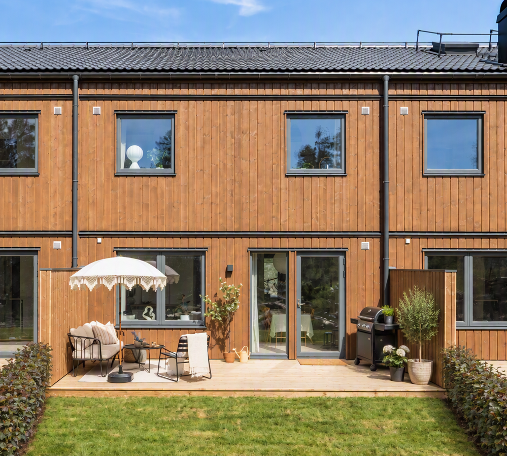 Uteplats med parasoll, utemöbler och grill intill radhusets träfasad.